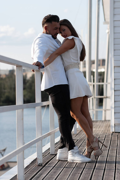 Couple aimant dans des tenues à la mode embrassant tout en se tenant au port avec des bateaux en été - Photo, image