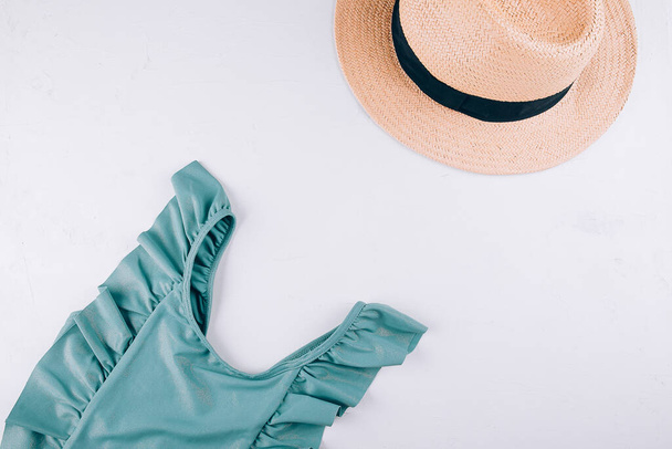 女性の夏の旅行ファッションの概念。ターコイズの水着、白い背景にストローバッグ。トップビュー、フラットレイアウト. - 写真・画像
