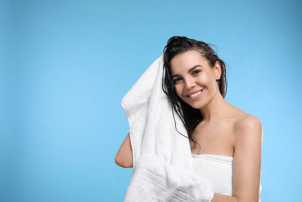 Happy young woman drying hair with towel after washing on light blue background. Space for text - Φωτογραφία, εικόνα