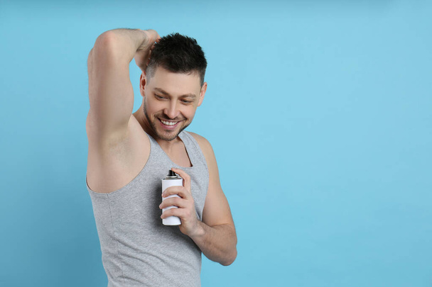 Handsome man applying deodorant on turquoise background. Space for text - Photo, Image