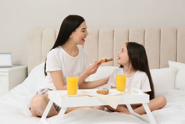 Young mother and her daughter having breakfast on bed at home - Fotoğraf, Görsel