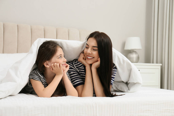 Young mother and her daughter under blanket in bed at home - Foto, Imagem