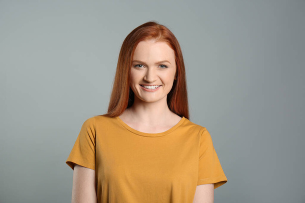 Candid portrait of happy young woman with charming smile and gorgeous red hair on grey background - Foto, Imagem