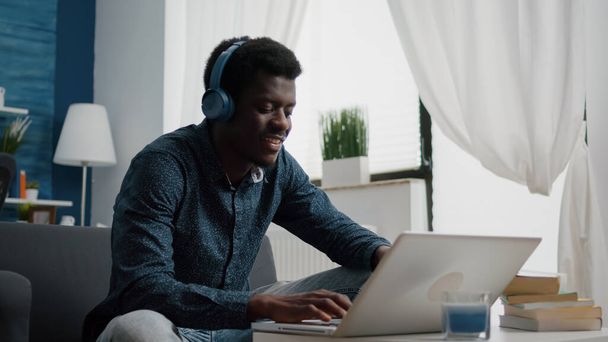ヘッドフォンを装着した黒人アフリカ系アメリカ人男性がノートパソコンに入力し - 写真・画像