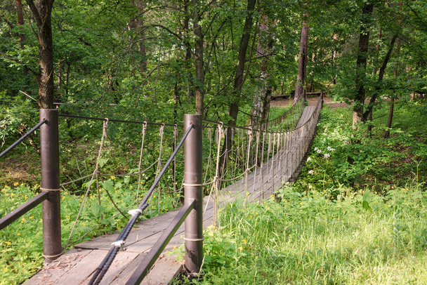 Suspension wooden bridge in the forest. Rope bridge suspended between two hills in the woods. - Photo, Image