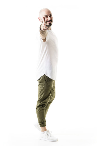 Seitenansicht eines fröhlichen, freundlichen jungen Mannes, der mit der Pistole auf die Kamera zielt. Volle Körperlänge isoliert auf weißem Hintergrund - Foto, Bild