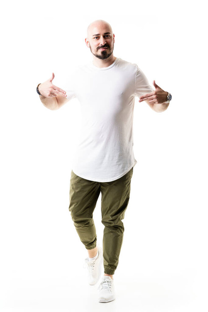Stylowy młody łysy brodaty mężczyzna celujący w reklamę pustej białej koszulki. Długość całego ciała odizolowana na białym tle - Zdjęcie, obraz