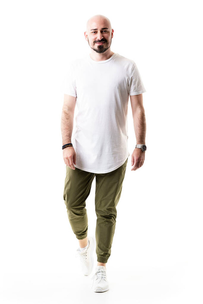 Boldog sétáló kopasz szakállas férfi olíva zöld nadrágban és üres fehér ingben. Teljes test hossza elszigetelt fehér háttér - Fotó, kép