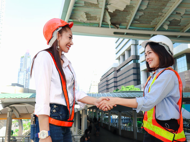 Kaksi nuorta kaunista aasialaista naisinsinööriä turvaliiveissä ja kypärässä kättelemässä keskusteltuaan projektityöstä kaupungin keskustan toimistossa.  - Valokuva, kuva