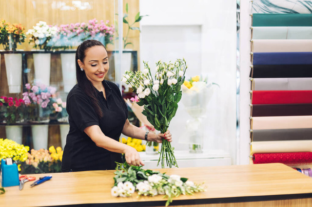 Een mooie vrouw bloemist maakt een compositie van bloemen in haar bloemenwinkel, boeket van bloemen - Foto, afbeelding