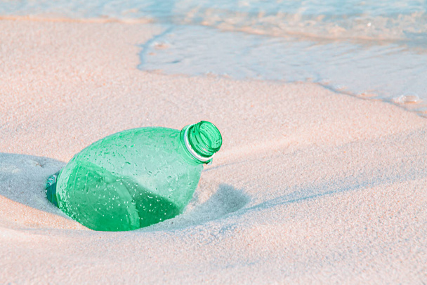 Közelről egy zöld műanyag vizes palack elásva a homokos tengerparton - Fotó, kép