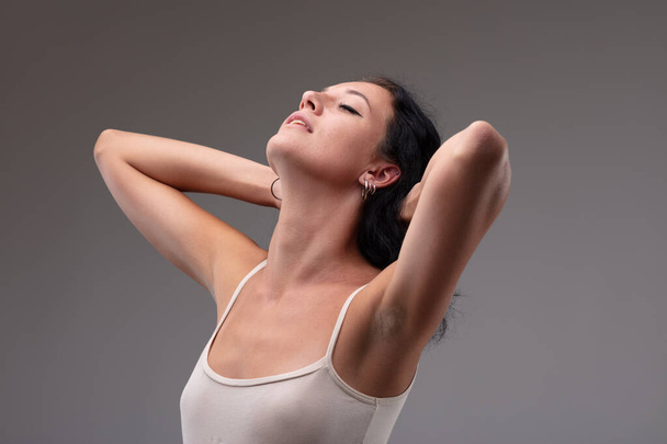 Serene young woman stretching back her head with parted lips and closed eyes with a blissful expression on a grey background - Photo, Image