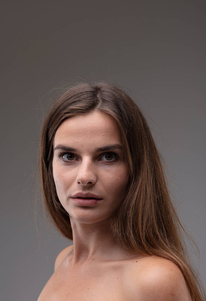 Intense beautiful young woman turning to stare at the camera with large wide open brown eyes and parted lips on a grey studio background - Photo, Image