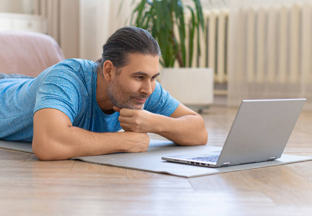 Мужчина среднего возраста дома перед ноутбуком во время онлайн видео-встречи с друзьями. - Фото, изображение