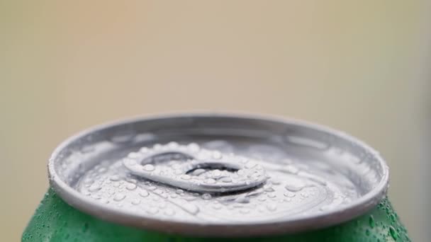 Giro, rotación: parte superior de la lata de aluminio con una cerveza fría u otra bebida cubierta con gotas de agua sobre un fondo borroso. - Metraje, vídeo