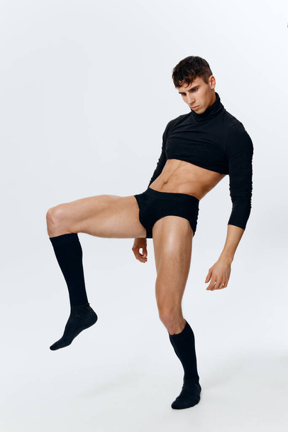 un atleta hombre en pantalones cortos, un suéter y calcetines levantó la pierna sobre un fondo claro - Foto, imagen