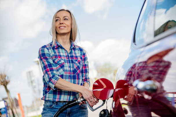 Smiling blonde woman is filling her car with gasoline at a gas station. - Foto, imagen