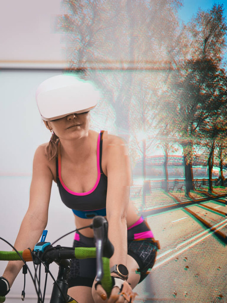 Vrouw traint thuis op een stilstaande fiets met VR-headset. - Foto, afbeelding