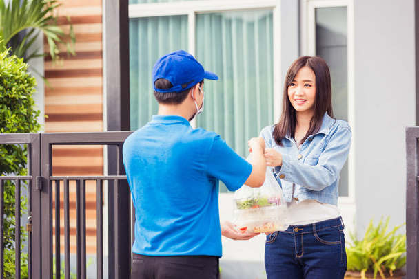 Asian young delivery man wear face mask he making grocery service giving rice food boxes plastic bags to woman customer receiving door at house after pandemic coronavirus, Back to new normal concept - Foto, imagen