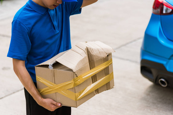 Asian young delivery man in blue uniform he emotional falling courier hold damaged cardboard box is broken at door front home, Accident bad transport shipment or poor quality delivery service concept - Photo, image