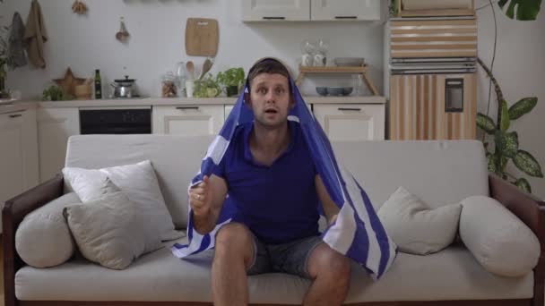 Tifoso greco di sport o calcio a casa con la bandiera della Grecia - Filmati, video