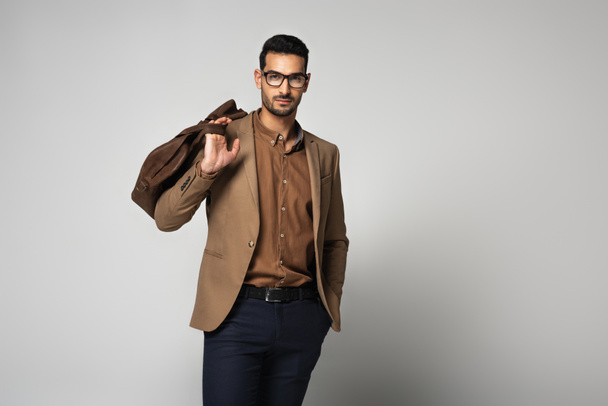 Мусульманский бизнесмен в очках держит сумочку на сером фоне - Фото, изображение