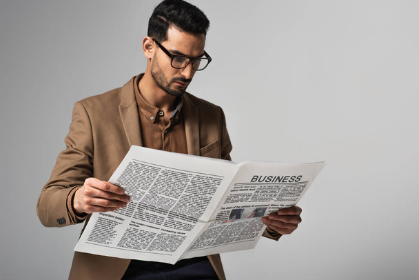 Arabischer Geschäftsmann in Anzug und Brille liest Wirtschaftsnachrichten isoliert auf grau - Foto, Bild