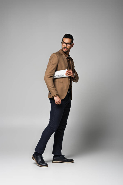 Arabian businessman in eyeglasses holding newspaper on grey background - Fotografie, Obrázek