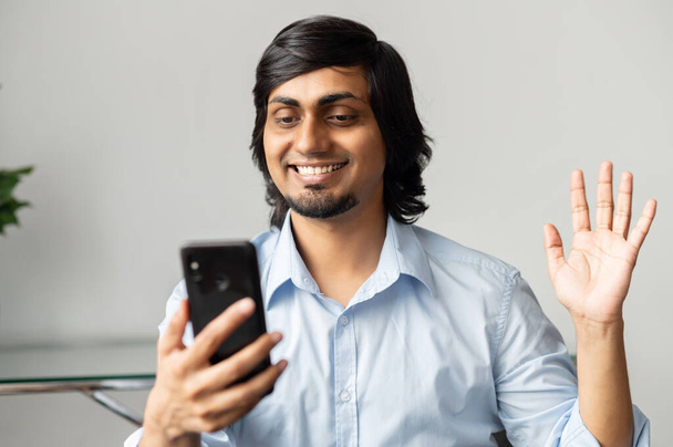 Contemporary cheerful indian colleague holding smartphone and waving hand - Fotografie, Obrázek