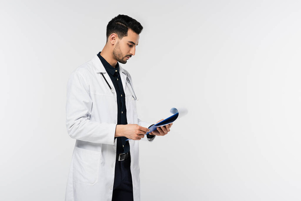 Vista laterale del medico arabo guardando appunti con carte isolate su grigio  - Foto, immagini