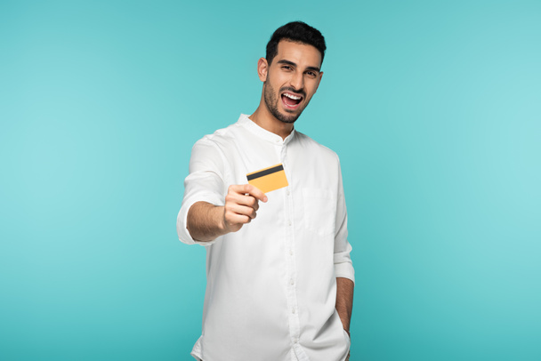 Fröhlicher arabischer Mann zeigt Kreditkarte isoliert auf blau  - Foto, Bild