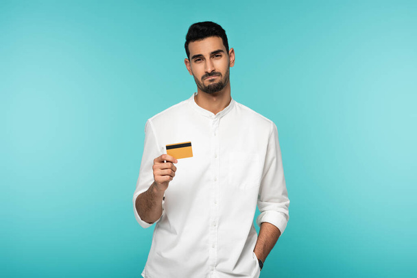 Displeased muslim man with credit card looking at camera isolated on blue  - Фото, изображение
