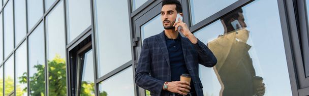 Arabský podnikatel mluví na smartphone a drží kávu jít blízko budovy, banner  - Fotografie, Obrázek