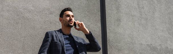 Young muslim businessman talking on mobile phone outdoors, banner  - 写真・画像