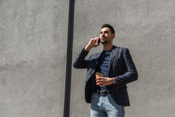 Молодий мусульманський менеджер розмовляє на мобільному телефоні і тримає чашку на відкритому повітрі
  - Фото, зображення