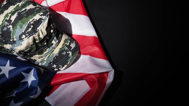 Americká vlajka a vojenský klobouk nebo taška. Horní úhel pohledu. Voják klobouk nebo helma s národní americkou vlajkou na černém pozadí. Reprezentovat vojenský koncept maskovacím objektem a vlajkou USA.  - Fotografie, Obrázek