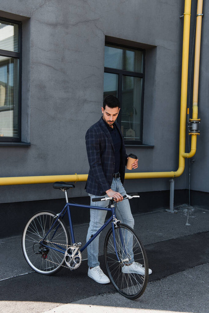 Arabian businessman holding bike and coffee to go outdoors  - Fotoğraf, Görsel