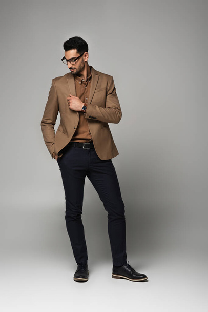 Arabian businessman in eyeglasses looking at jacket on grey background  - Photo, Image