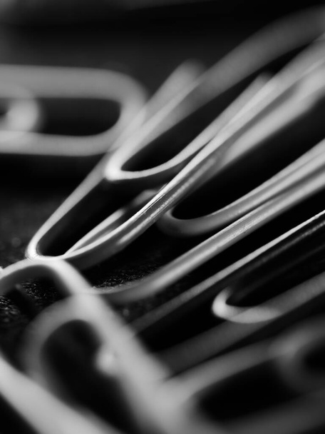 A vertical grayscale shot of scattered paperclips on a black surface - Foto, Imagem