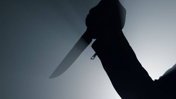 Siluet adam karanlıkta bıçak tutuyor. Suçlu eli hançerle saldırıyor..  - Fotoğraf, Görsel