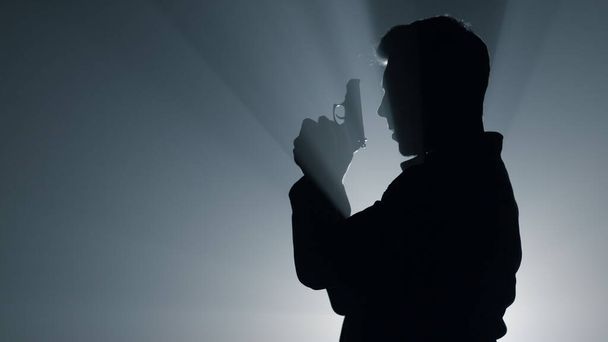Silhouette skupił człowieka strzelającego w ciemności. Karny celownik z pistoletu. - Zdjęcie, obraz