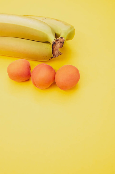 A vertical shot of ripe bananas and apricots isolated on yellow background - Fotoğraf, Görsel