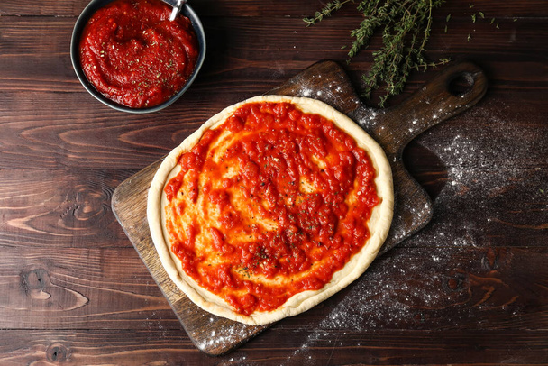 Pâte à pizza avec sauce tomate savoureuse sur fond de bois - Photo, image