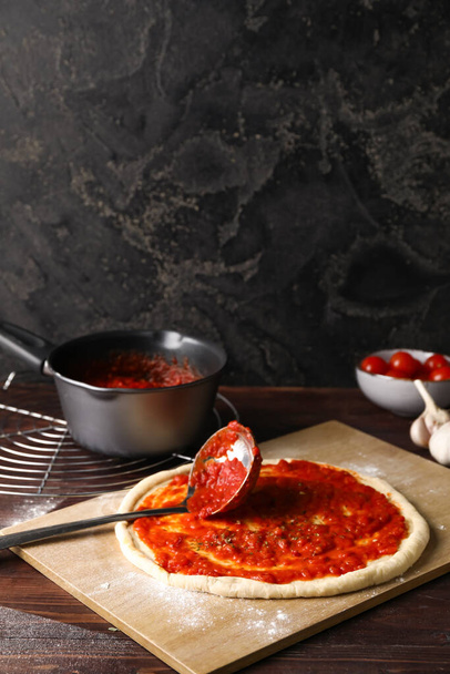 Pizza dough with tasty tomato sauce on dark background - Photo, image