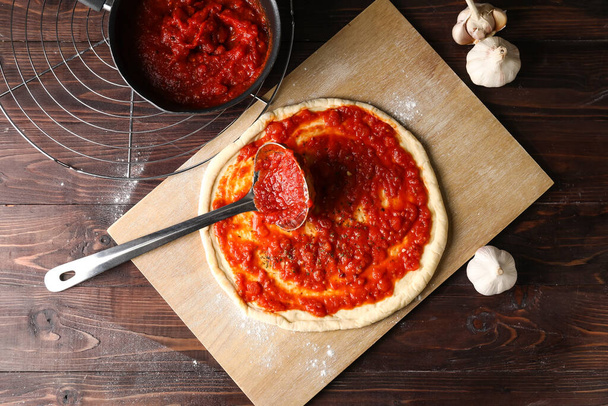 Pâte à pizza avec sauce tomate savoureuse sur fond de bois - Photo, image