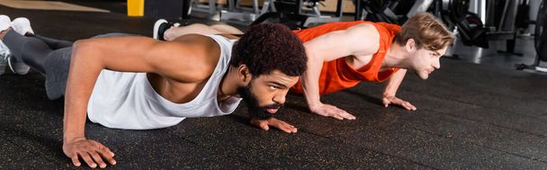 hombres interracial en ropa deportiva haciendo flexiones en el centro deportivo, pancarta - Foto, Imagen