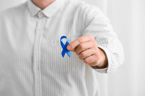 Man with blue ribbon on light background, closeup. Cancer awareness concept - Photo, image