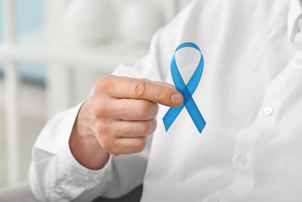 Man with blue ribbon in clinic, closeup. Prostate cancer awareness concept - Фото, изображение