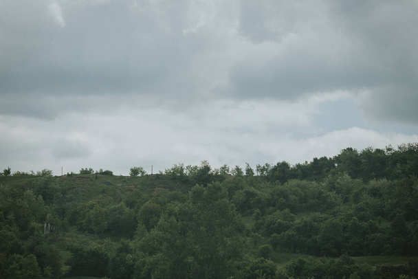 Ein düsterer Tag auf dem Land mit regnerischen grauen Wolken über dicken grünen Bäumen am - Foto, Bild