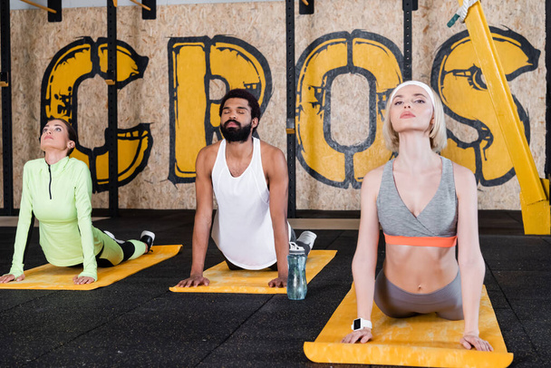 młodzi międzyrasowe ludzie medytujący w kobra poza w siłownia - Zdjęcie, obraz